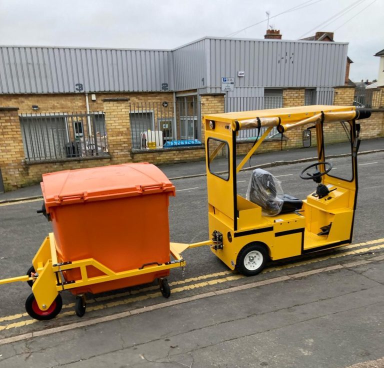 Electric industrial tug towing large waste container outdoors
